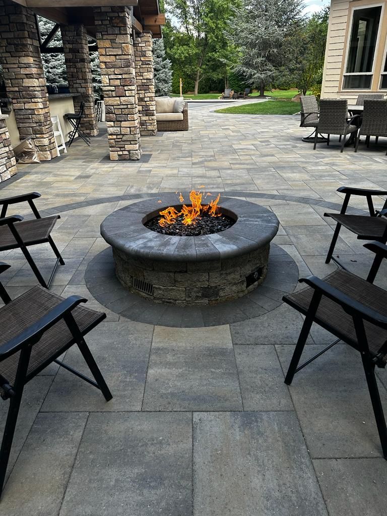 Stone patio with a circular fire pit and lounge chairs in an outdoor seating area