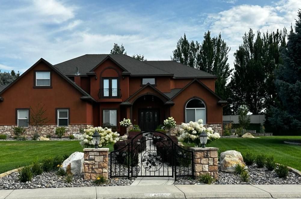 Brick house with stone gate, white flowers, and a manicured front yard under a cloudy sky