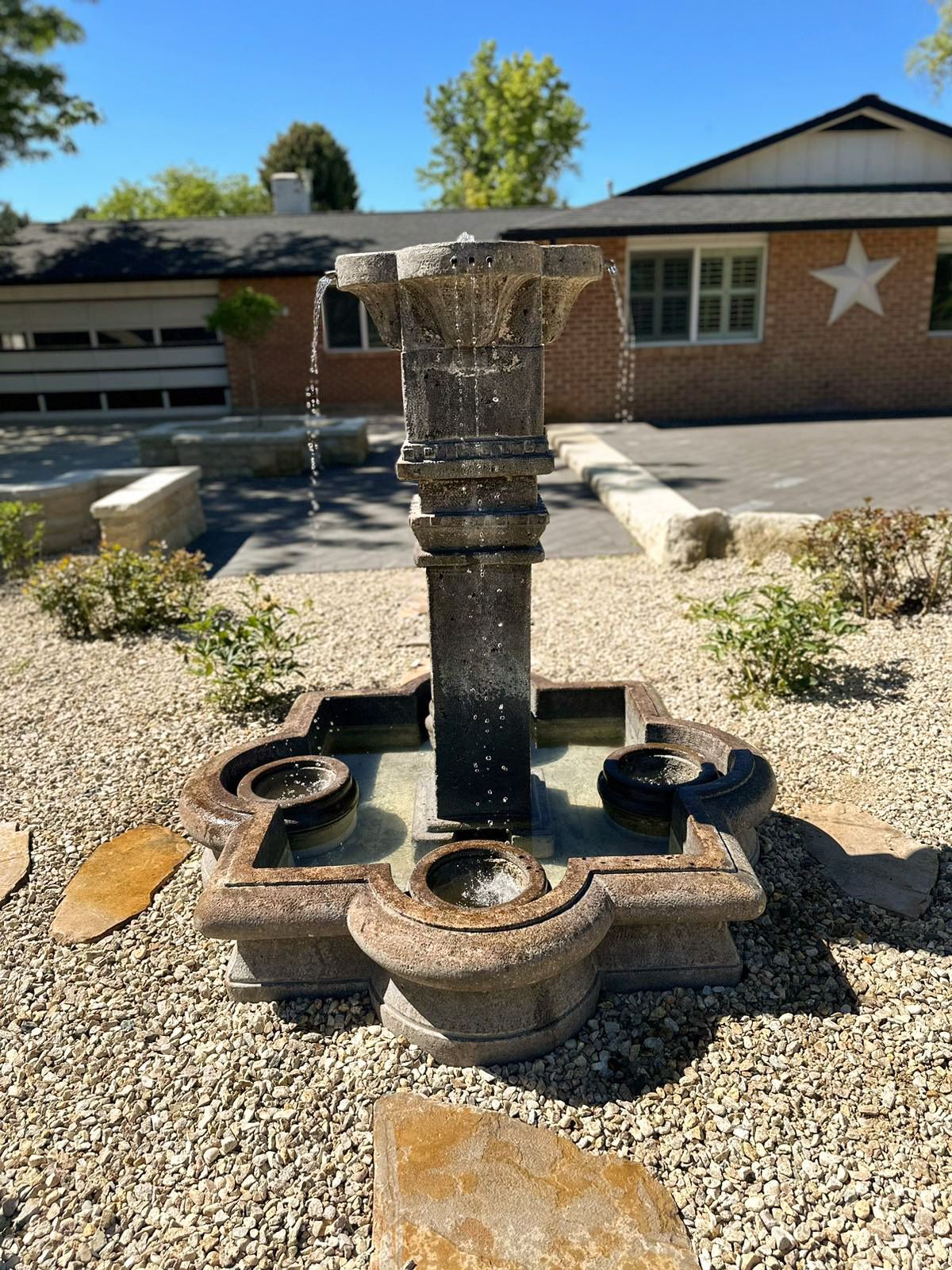 Decorative fountain in a gravel courtyard outside a brick building with a star on the wall.