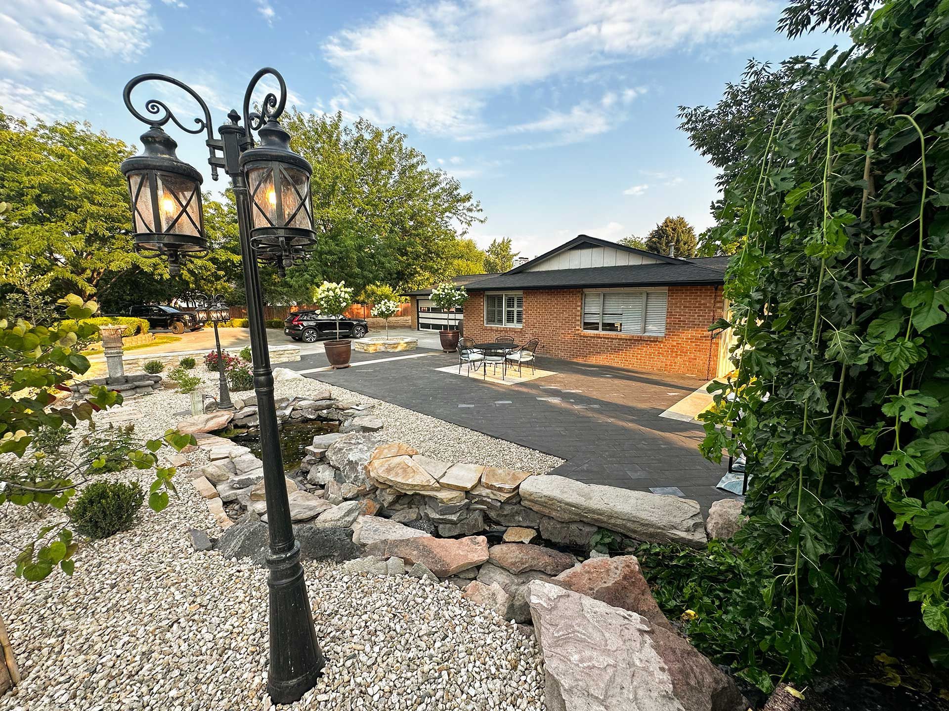 Stone patio with black lanterns, brick building, and garden greenery under a blue sky