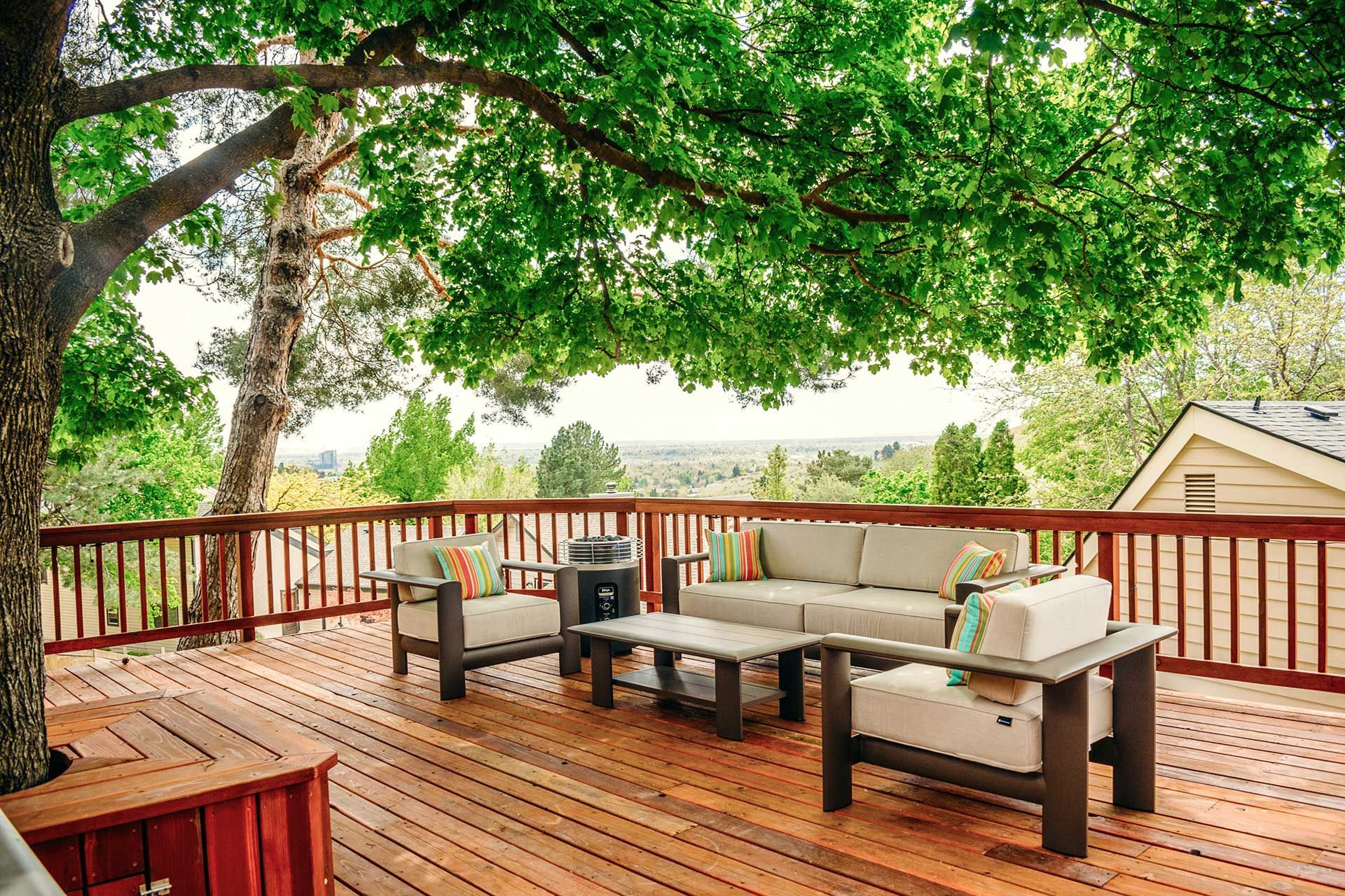 Wooden deck with cushioned outdoor seating under a leafy tree canopy