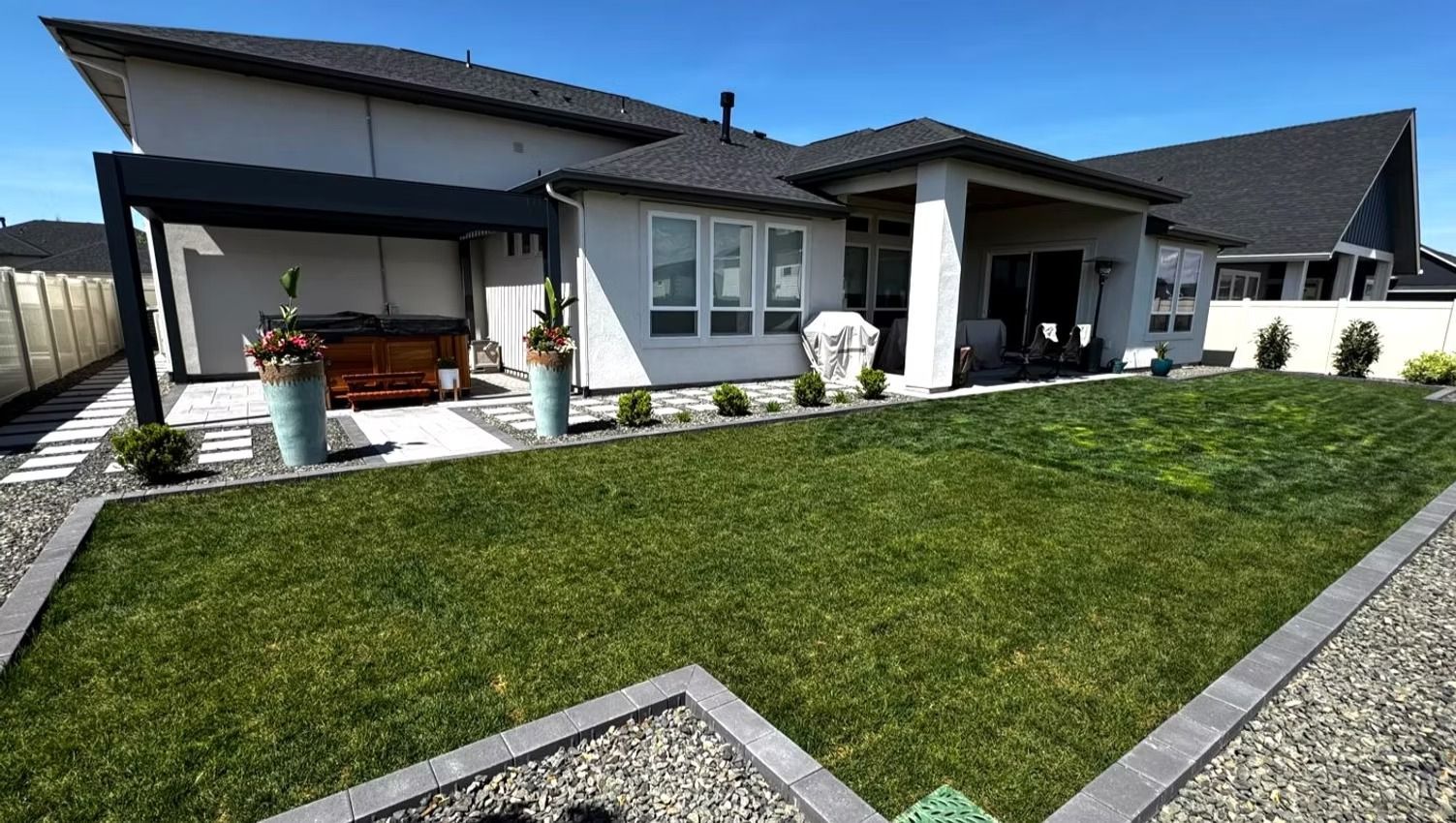 Modern single-story house with a sloped green lawn and patio under a cloudy sky