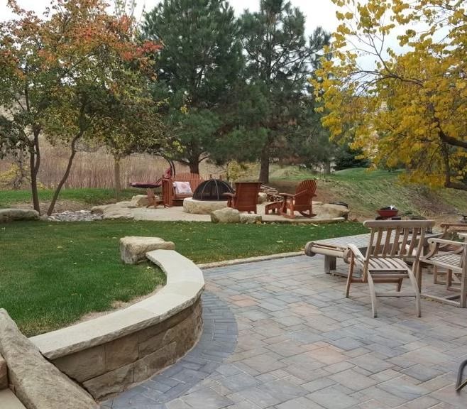 Stone patio with wooden chairs, fire pit, and trees in an autumn backyard setting