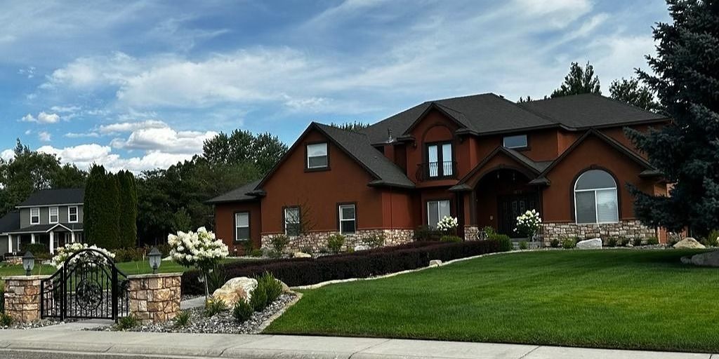 Large brick suburban house with manicured lawn, stone landscaping, and blue sky