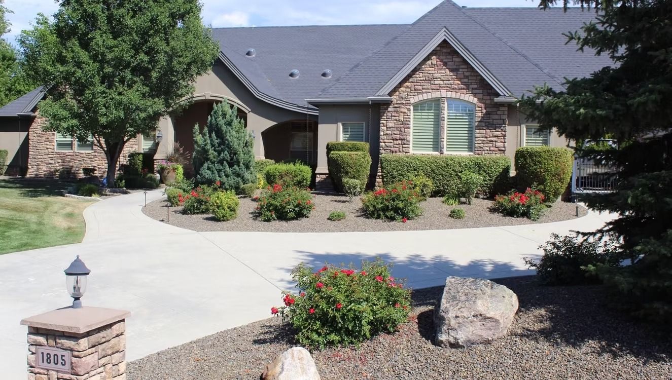 Suburban brick house with arched entry, flower beds, and a curved driveway under a clear sky