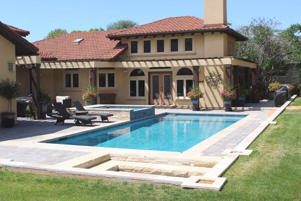 Backyard with a swimming pool beside a tan stucco house and red tile roof