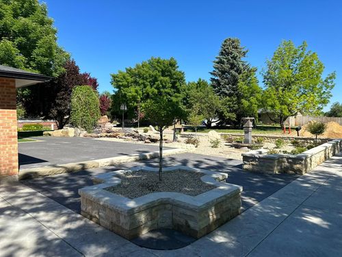 Sunny courtyard with stone benches, trees, and paved walkways beside a brick building