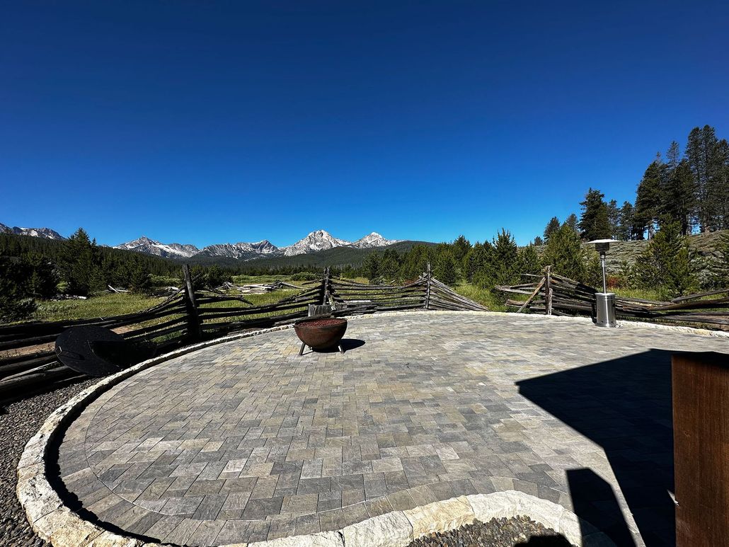 Patio with stone paving and potted plant overlooking green landscape and snow-capped mountains under a clear blue sky