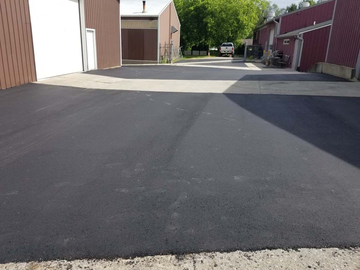 Newly paved black asphalt driveway between industrial buildings.