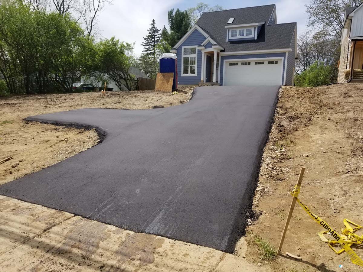 Newly paved asphalt driveway leading to a blue house with a garage.