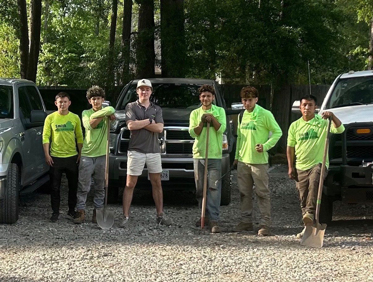 Five people in neon green shirts pose outdoors between parked trucks, one holding a shovel.