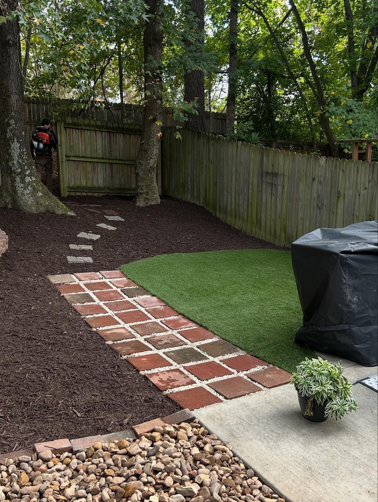 Backyard with brick path, gravel beds, wooden fence, lawn, and covered grill.