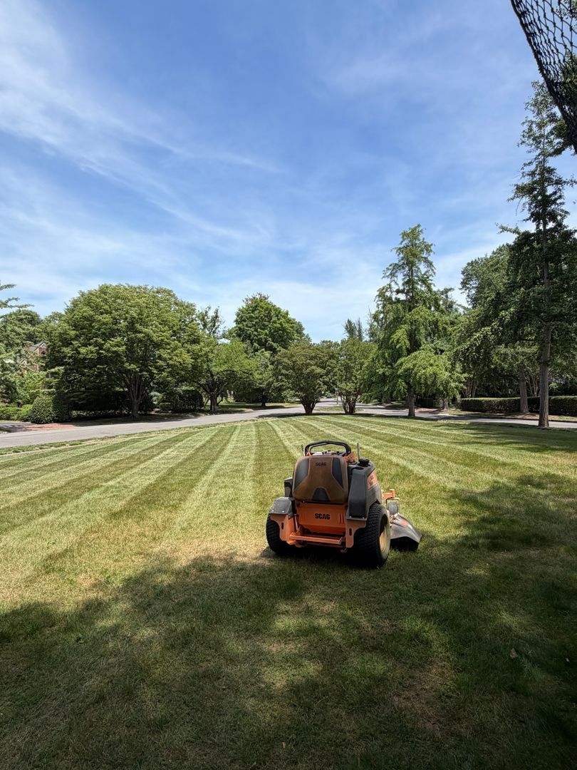 Orange lawn mower on a freshly cut grassy field with trees and blue sky in the background