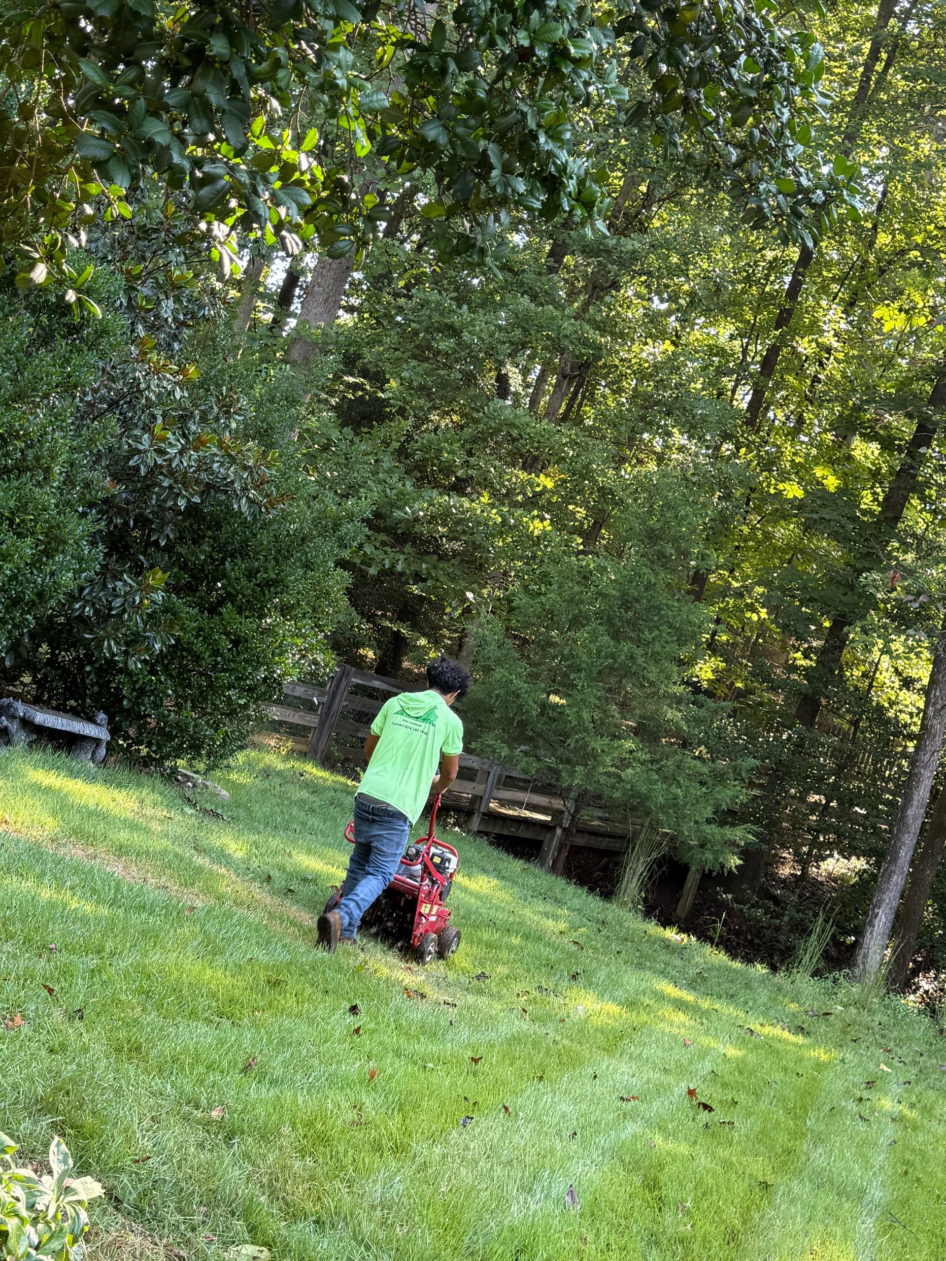 Person in a neon green shirt stands beside a red stroller on a grassy lawn under trees.