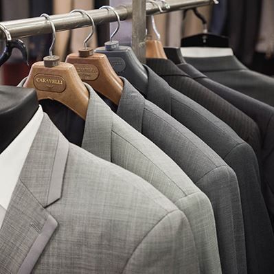 A row of suits are hanging on a rack in a store.