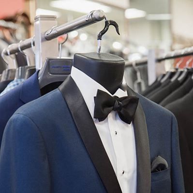 A blue tuxedo with a black bow tie is hanging on a mannequin.