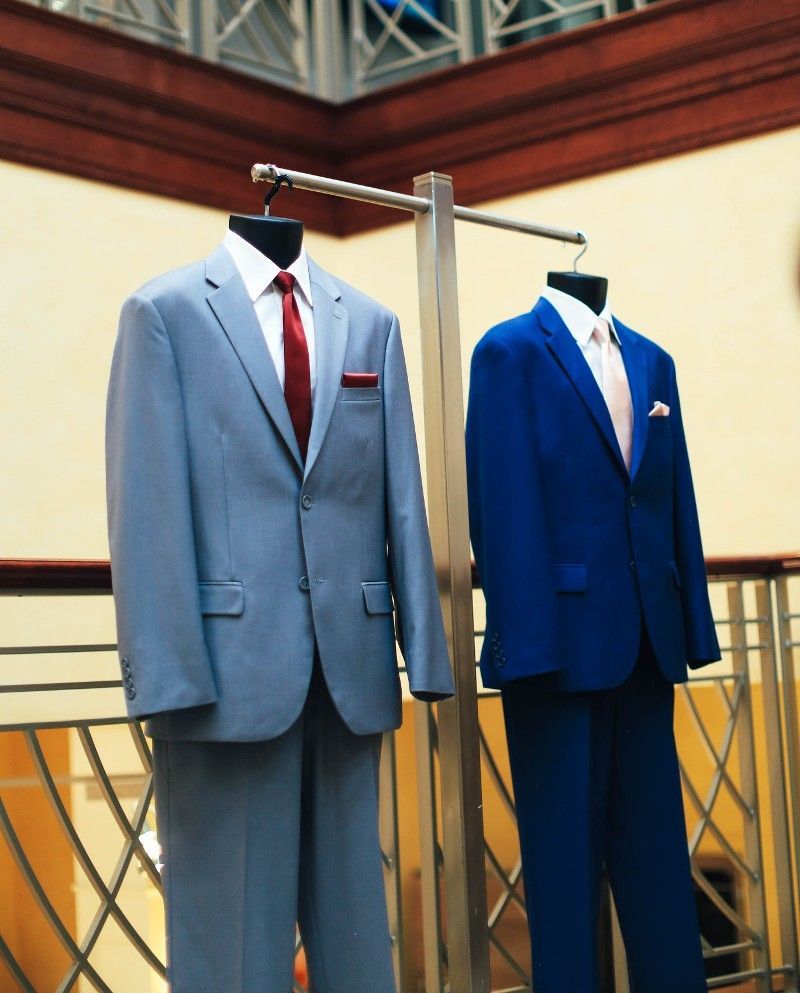 A grey suit and a blue suit are hanging on a rack