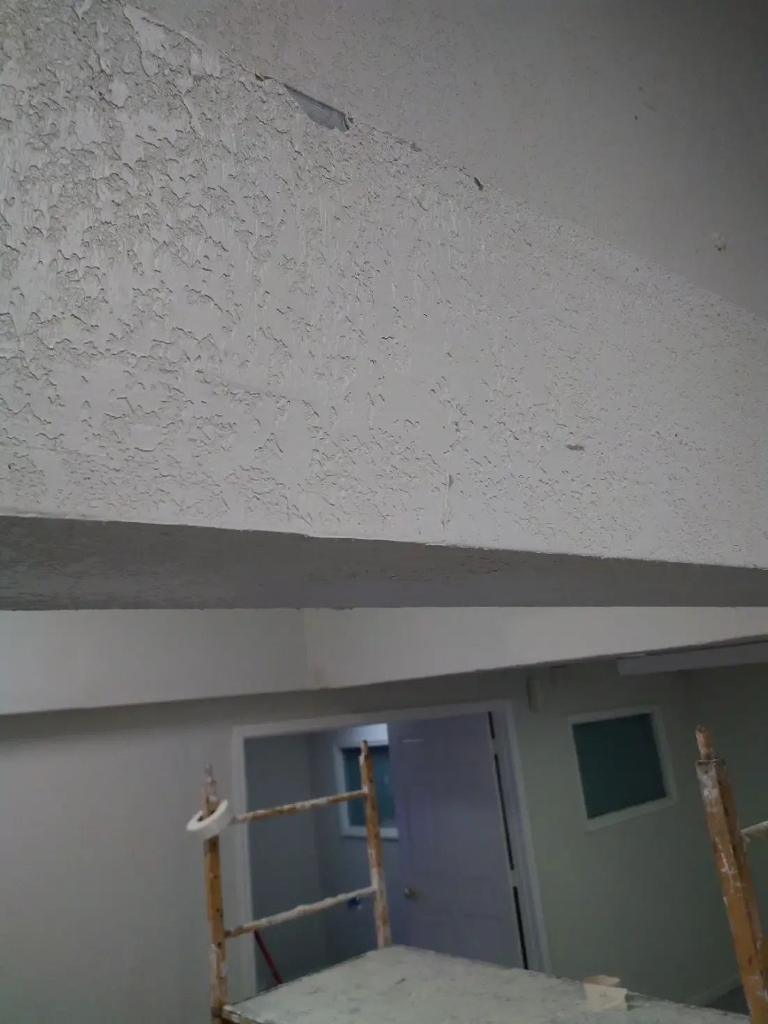 Indoor construction area with textured ceiling, scaffold, and a blue door under renovation