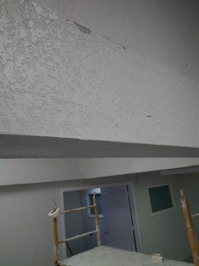 Indoor construction area with scaffold, door, and textured ceiling or wall plastering in progress