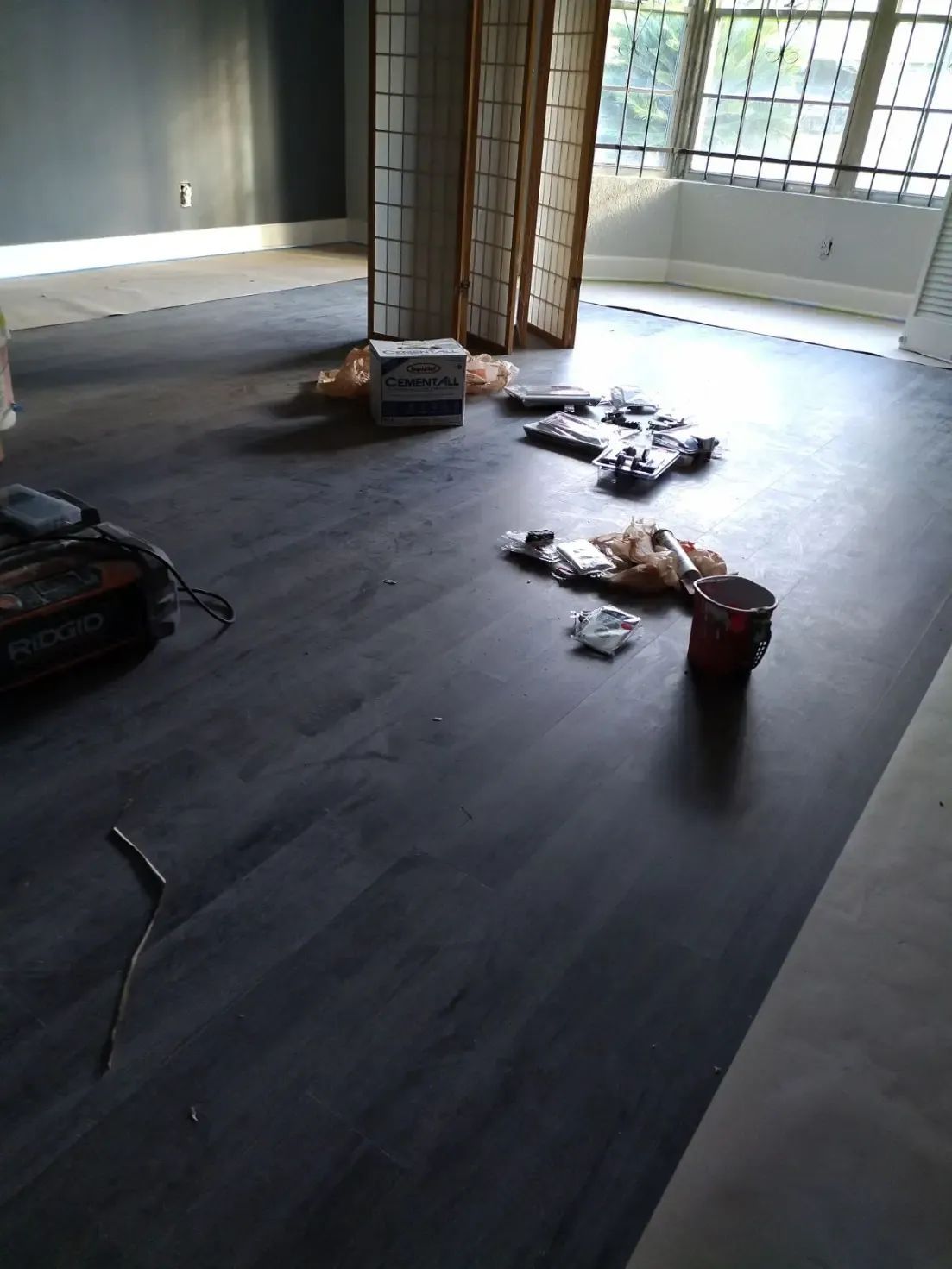 Empty room with dark flooring, window light, and scattered tools and supplies on the floor