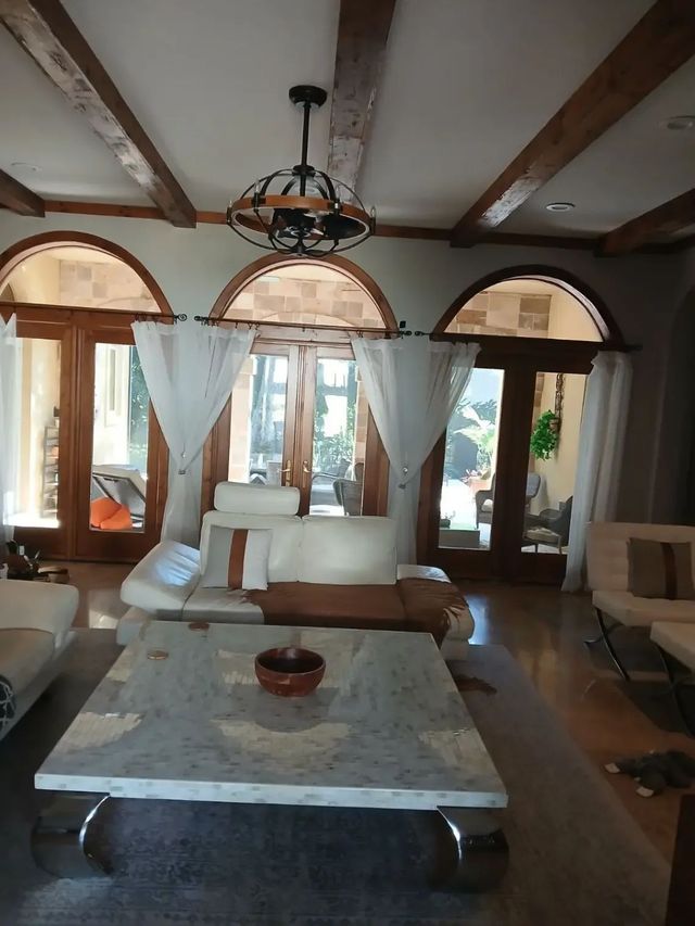 Bright living room with arched windows, white sofas, and a marble coffee table under exposed beams.