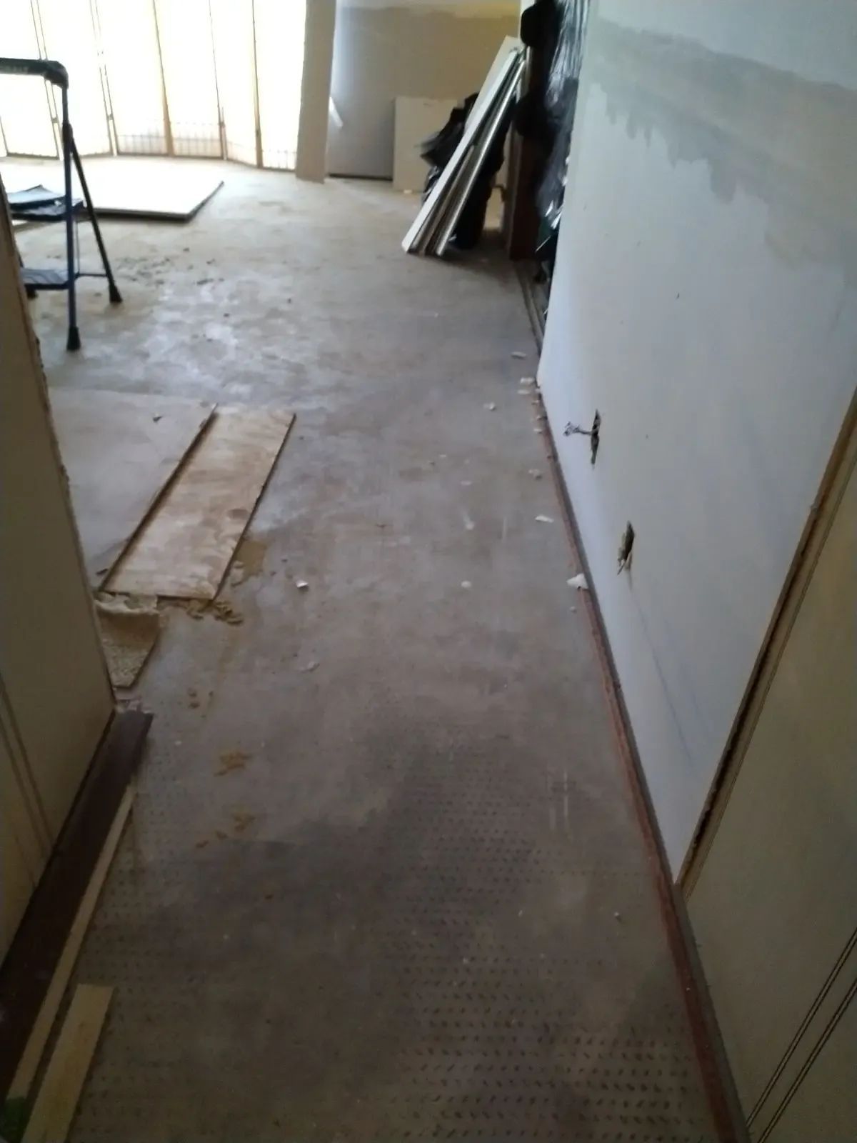 Unfinished hallway with bare drywall, concrete floor, and stacked boards near a doorway.