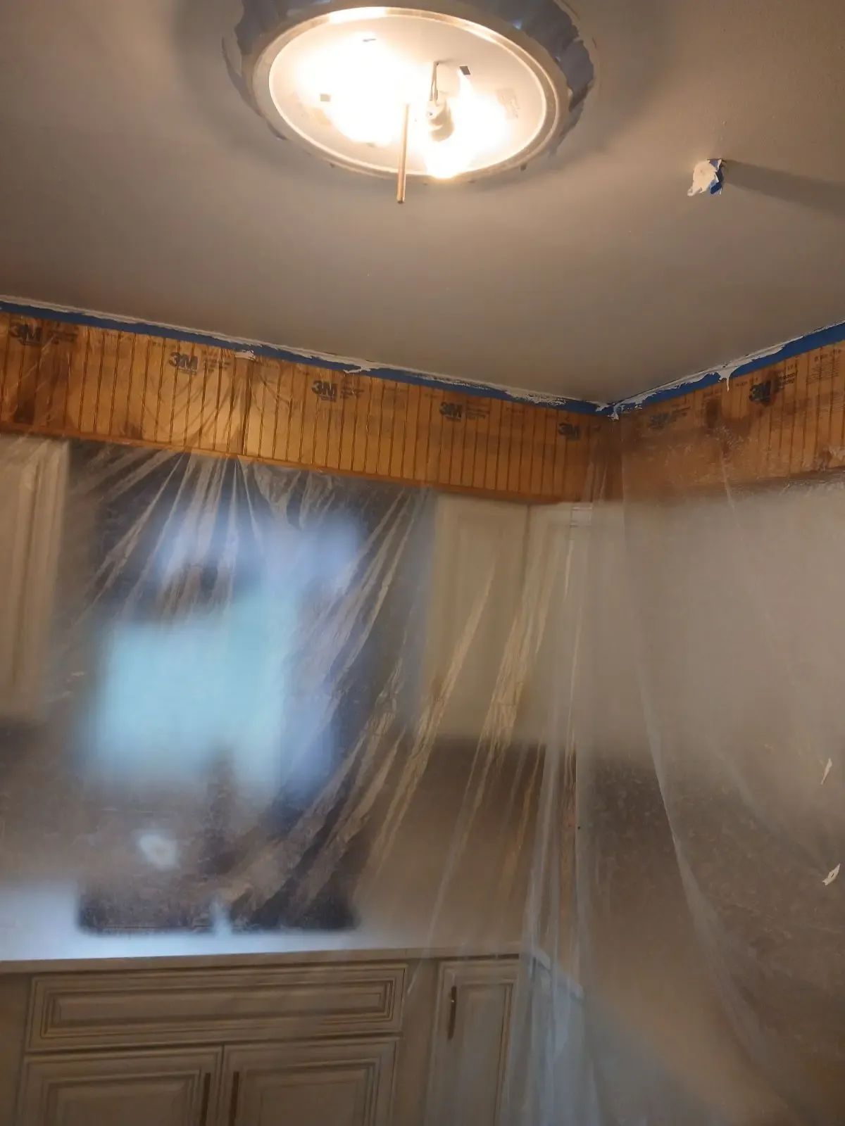 Bedroom with plastic-covered walls and ceiling during renovation, lit by a ceiling light.