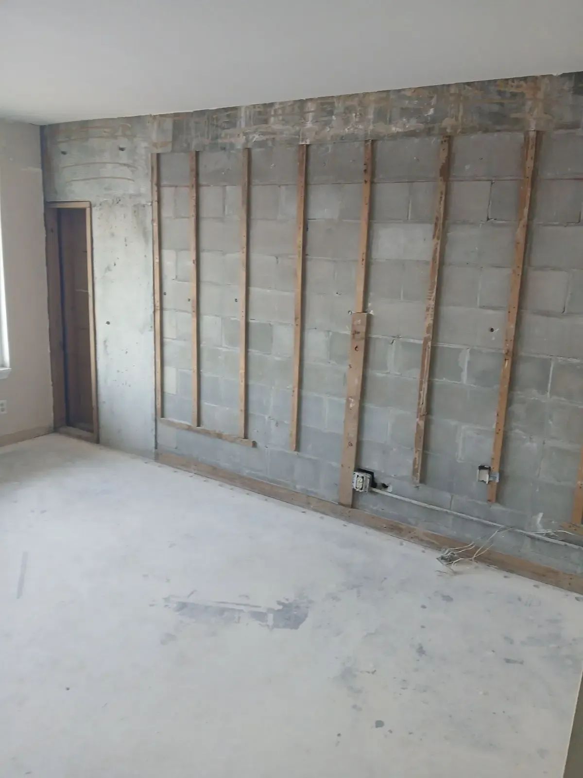 Unfinished room with exposed wall studs, gray block wall, and bare concrete floor