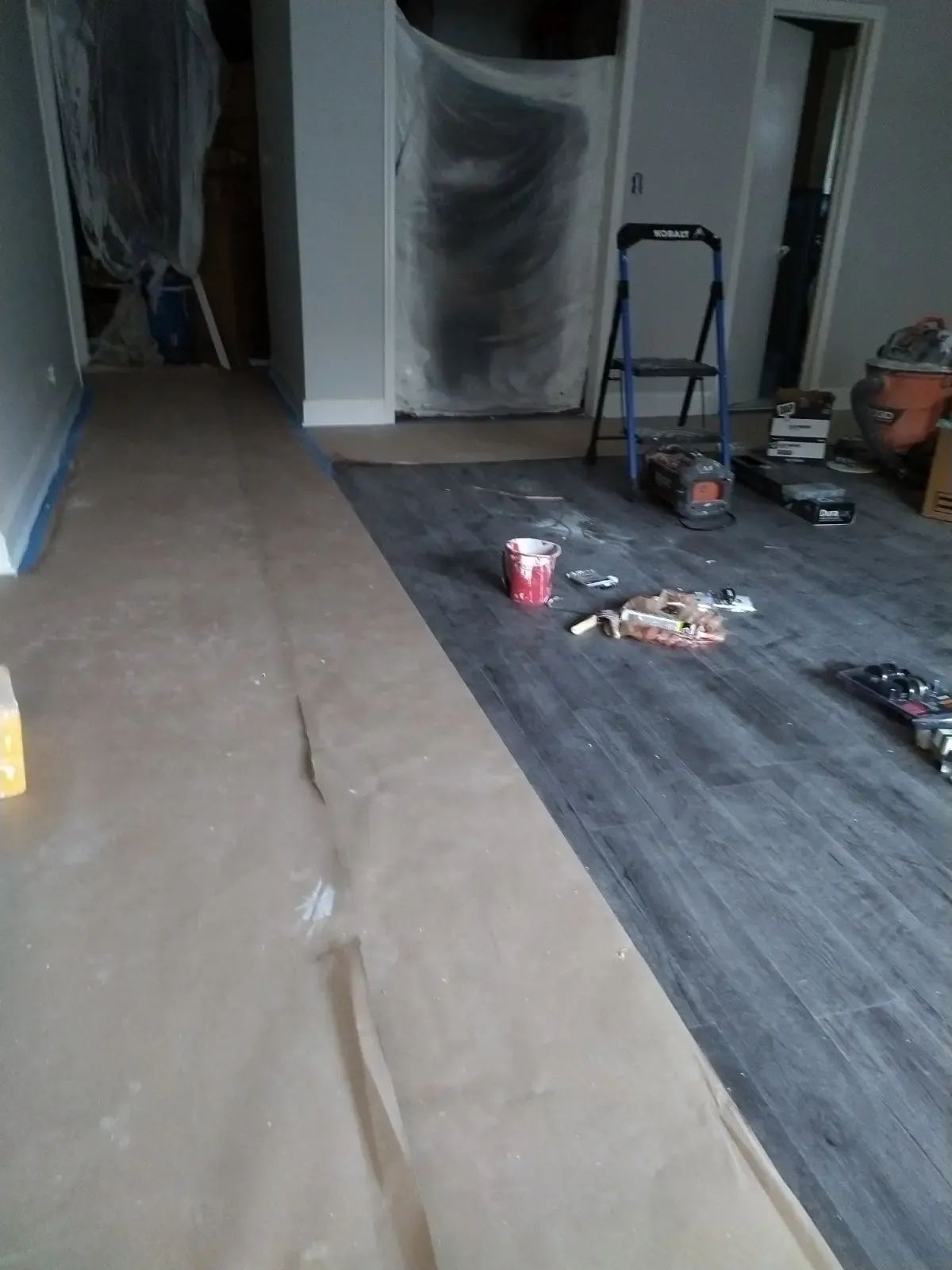 Renovation area with plastic-covered doorways, floor protection, and tools scattered on a partially finished floor