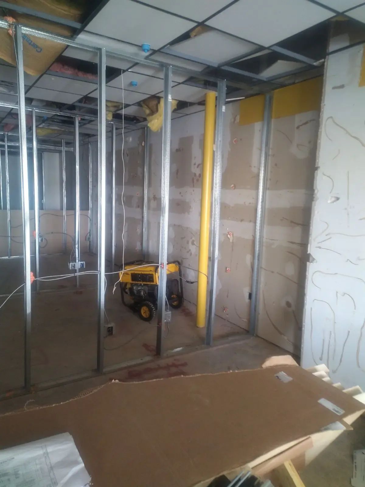 Unfinished room with metal wall framing, exposed ceiling, and a yellow tool on the floor.