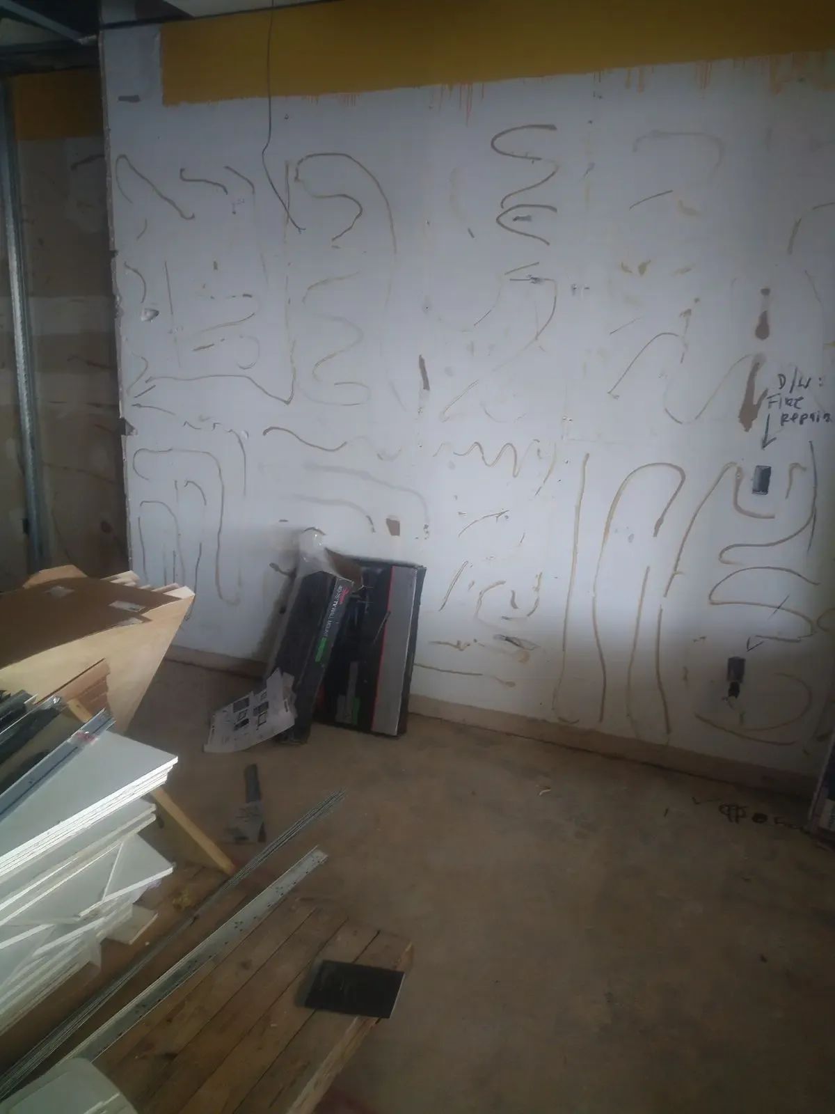 Partially painted white wall with faint pencil sketches in a cluttered room with stacked boards and tools