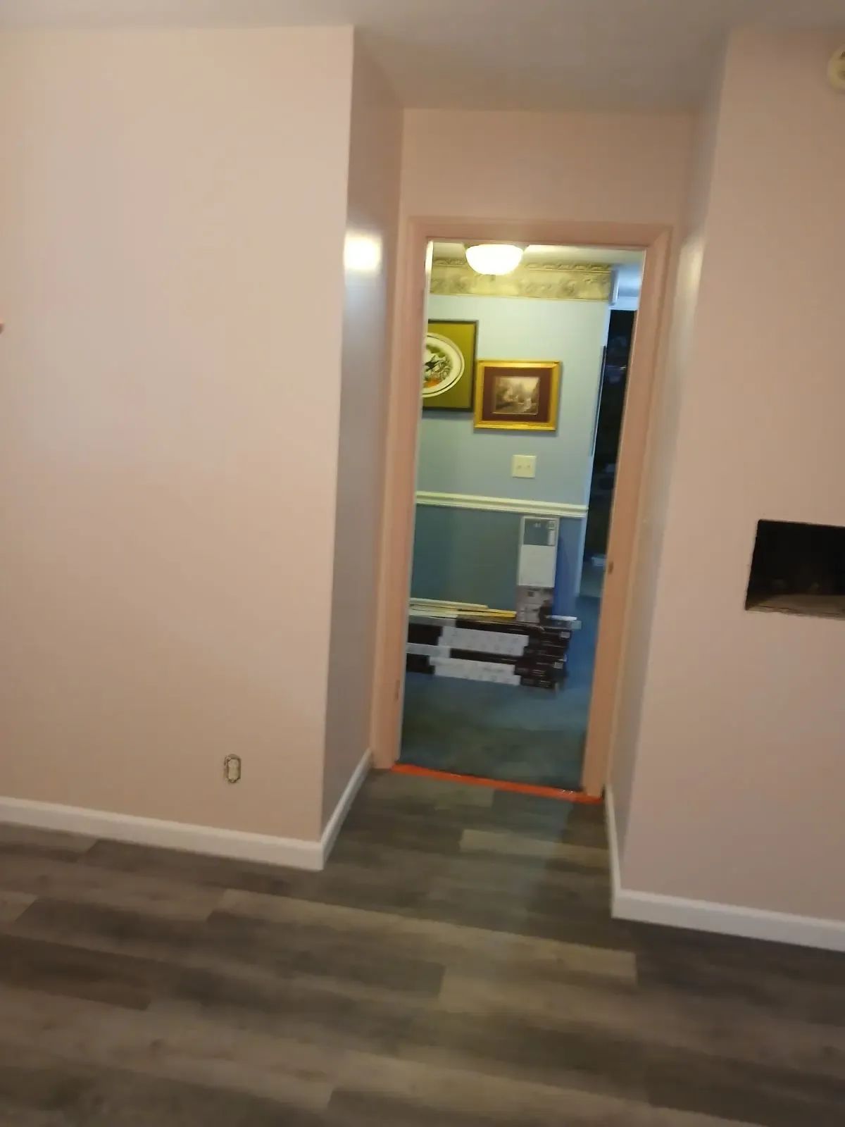 Empty hallway with gray flooring leading to a blue room framed by beige walls.