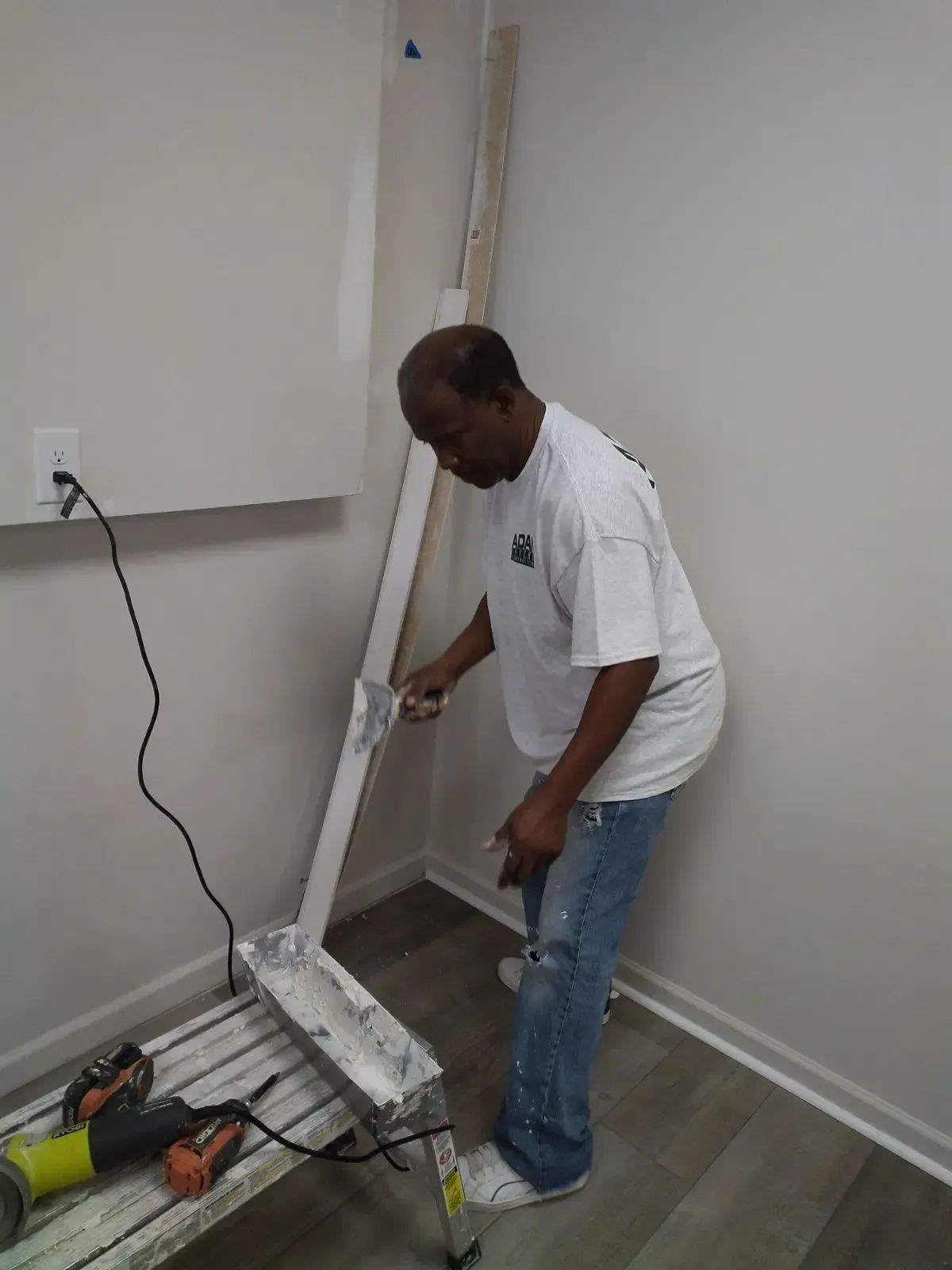 Man painting a wall trim in a mostly empty room with tools on the floor.