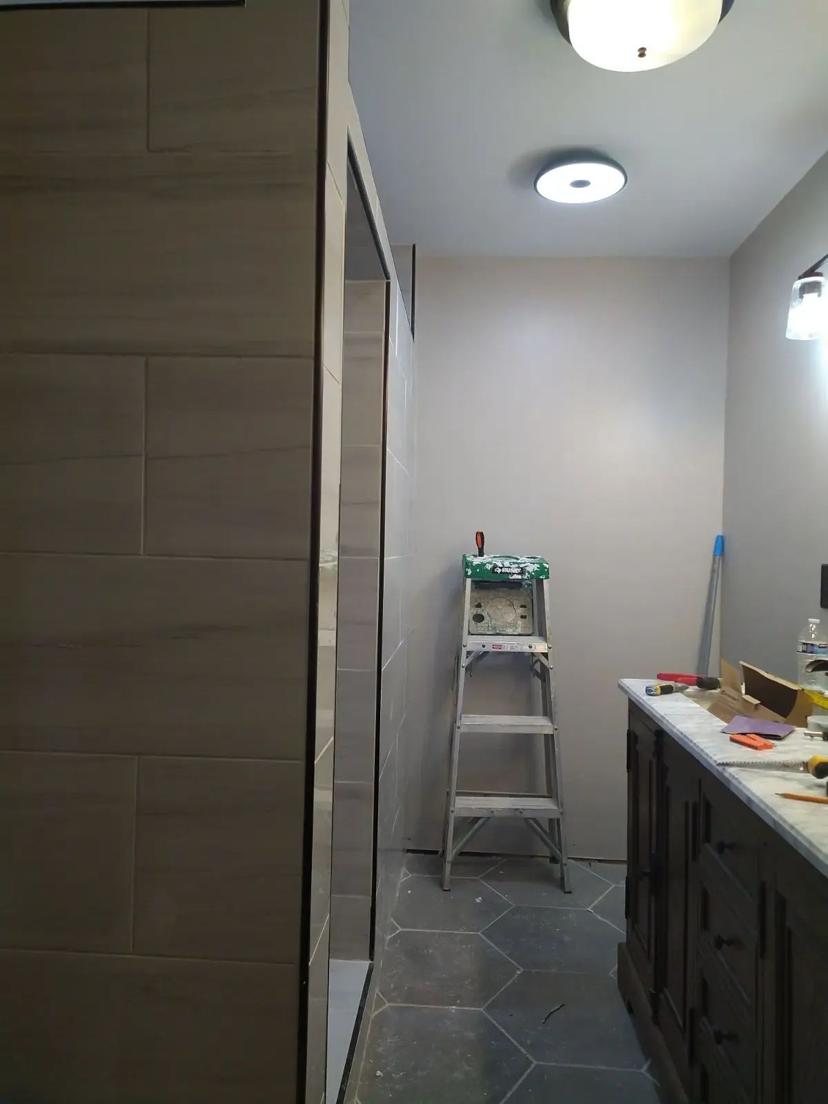 Narrow laundry room with a step ladder, dark cabinets, and white walls under ceiling lights.