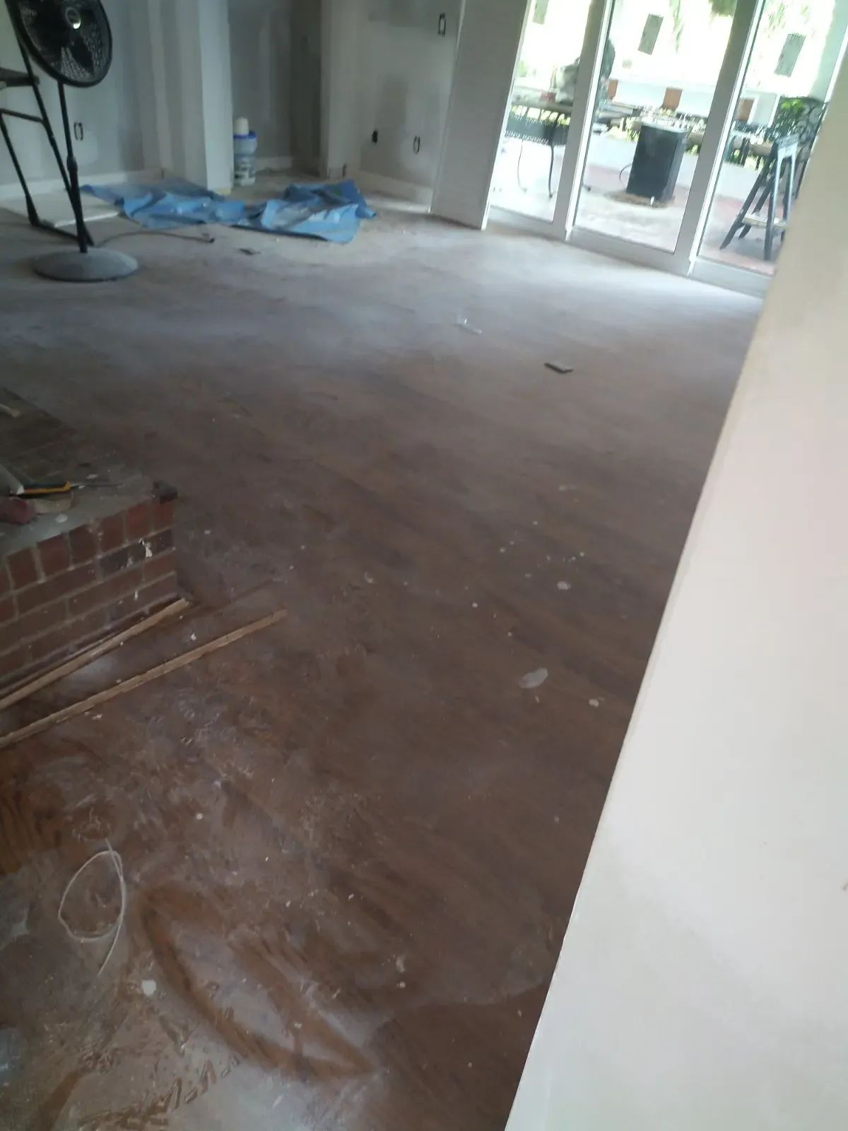 Empty room with dusty concrete floor, blue tarps near glass doors, and a white wall