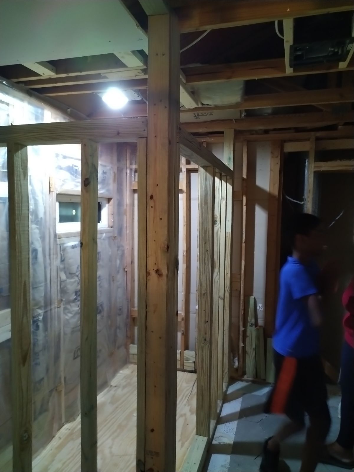 Narrow unfinished hallway with exposed wood framing and a person in a blue shirt walking through.