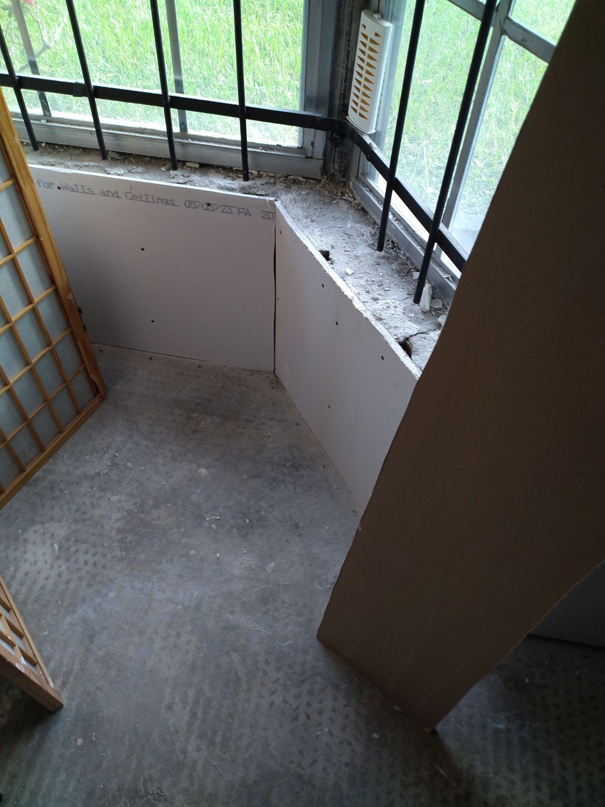 Empty concrete stairwell landing with white walls and black metal railing by a window.