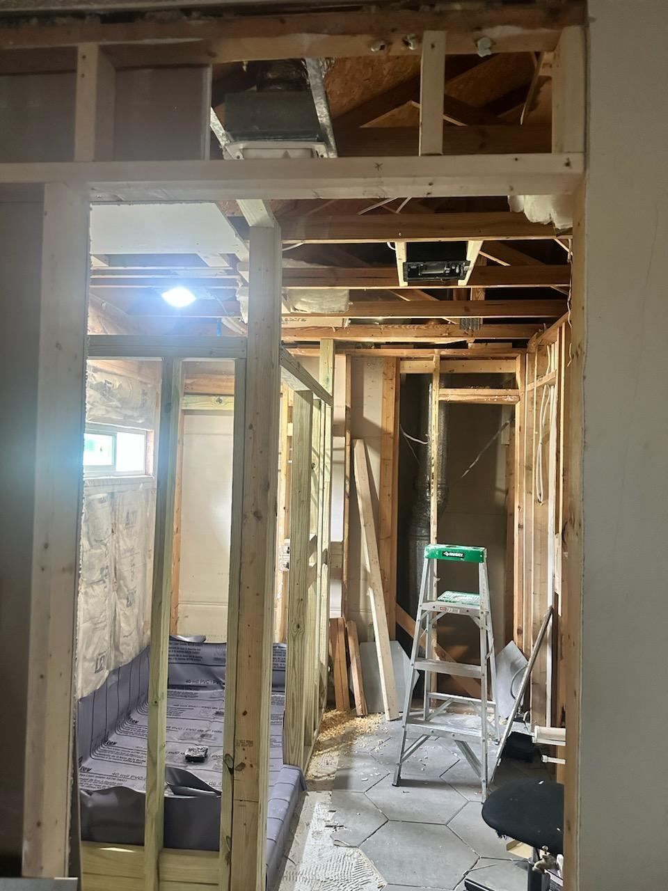 Narrow hallway under construction with exposed wooden framing, debris, and a ladder in the center.