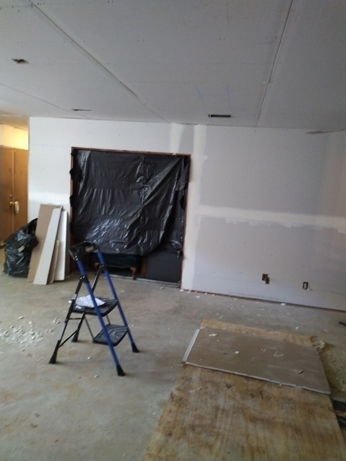 Partially renovated room with a ladder, covered doorway, and unfinished floor