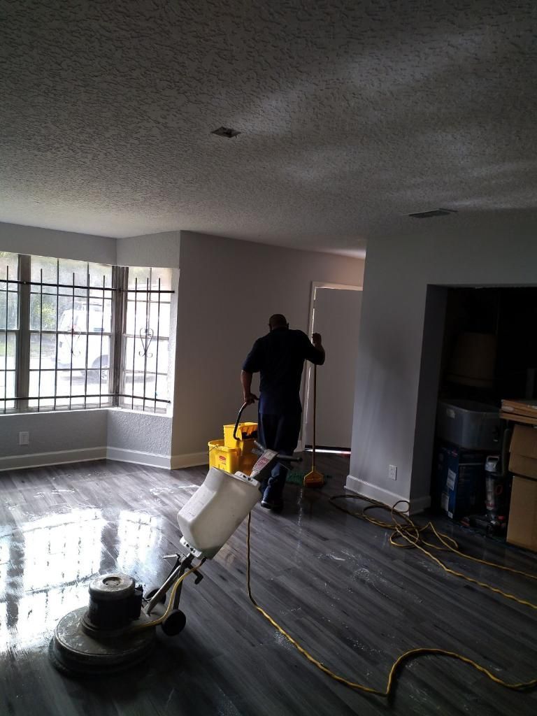 Person using a floor buffer in a room with wet floors and large windows.