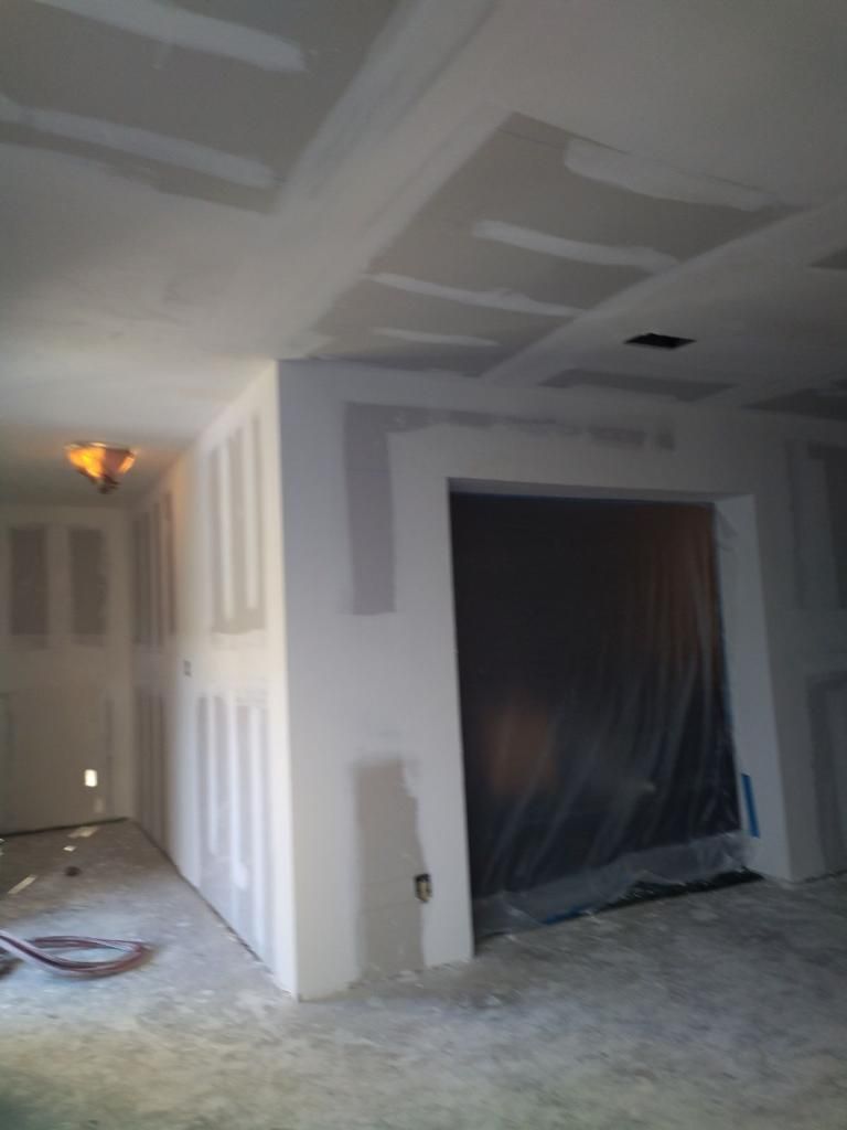 Unfinished interior room with drywall, plastic-covered doorway, and construction debris on the floor.