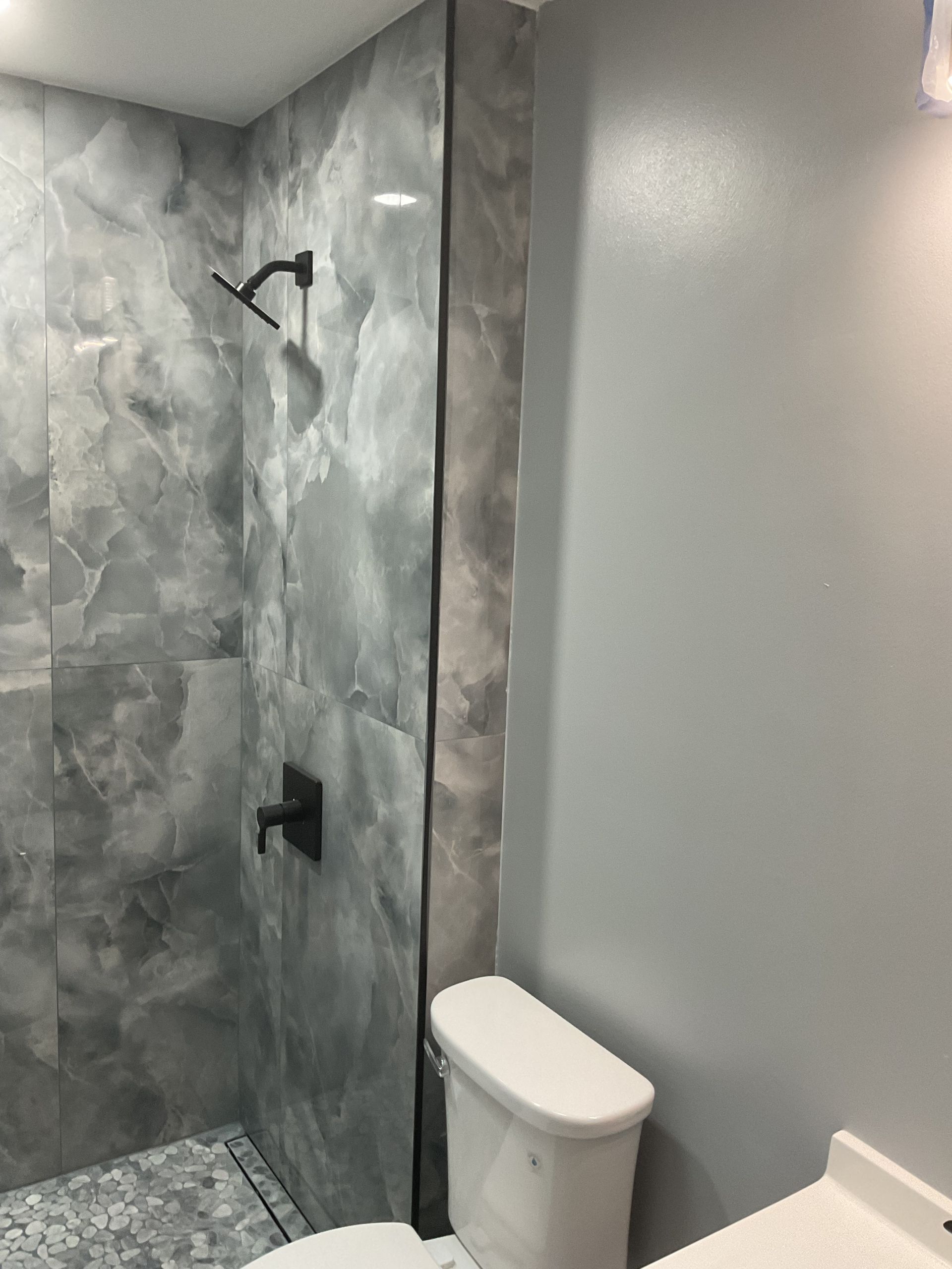 Small modern bathroom with gray tile shower, frosted glass wall, and white toilet