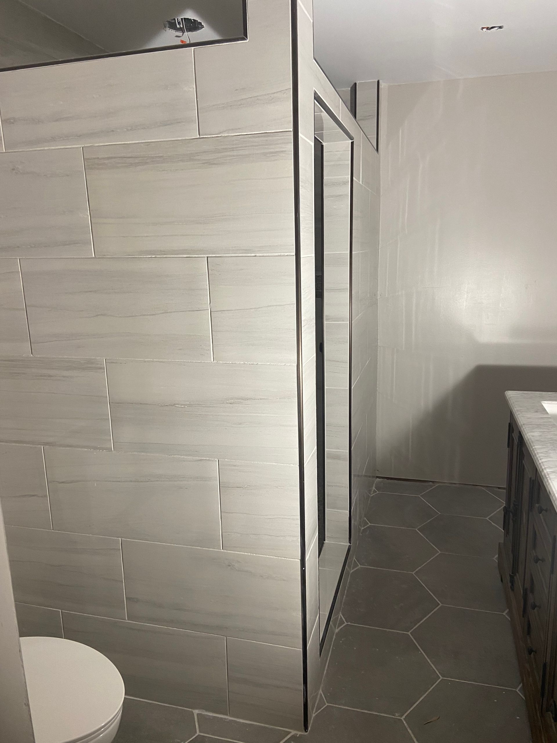 Bathroom with tiled shower stall, hexagon floor tiles, and white walls.