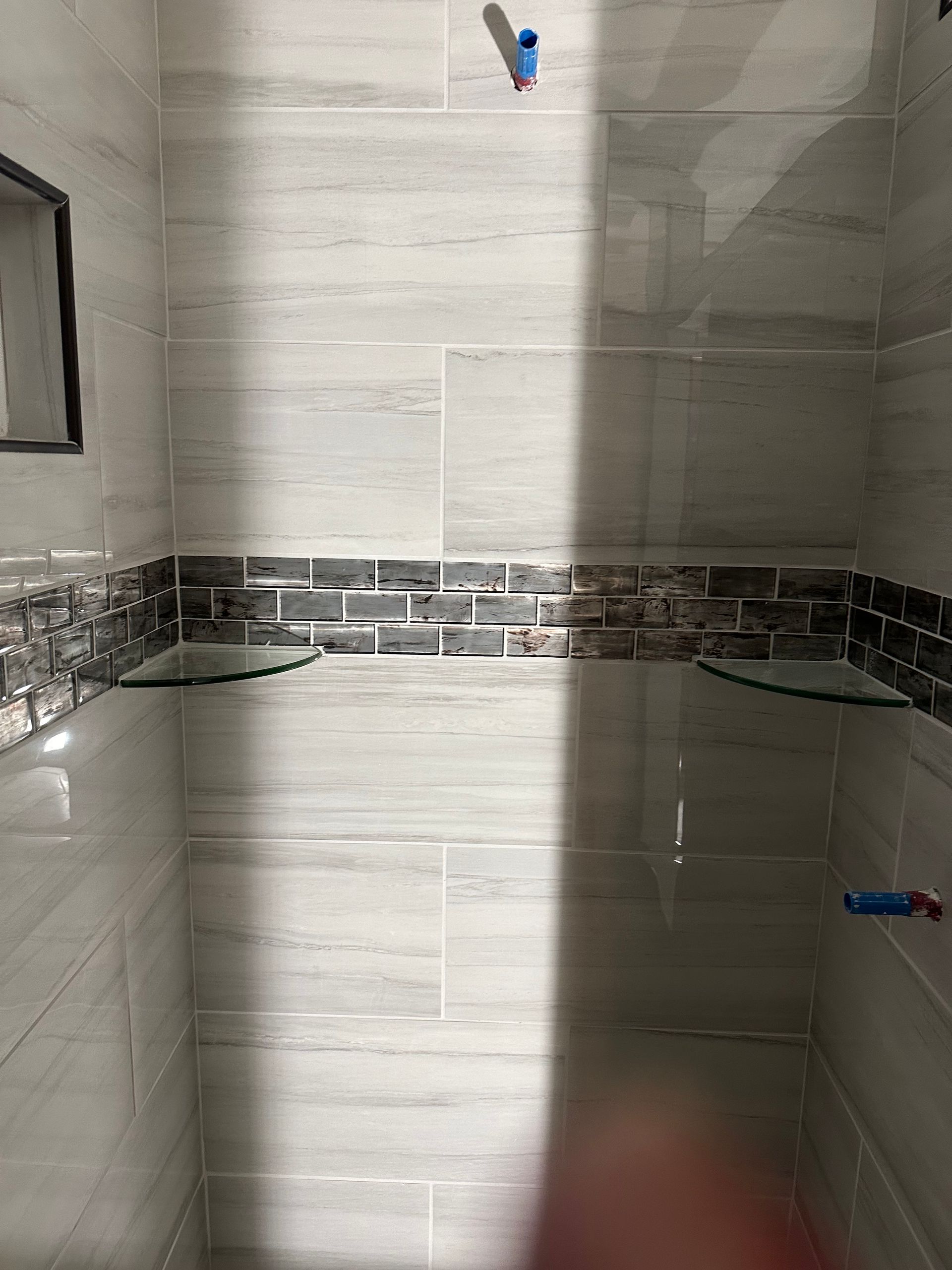 Shower stall with light gray tile and a dark decorative mosaic band around the walls.