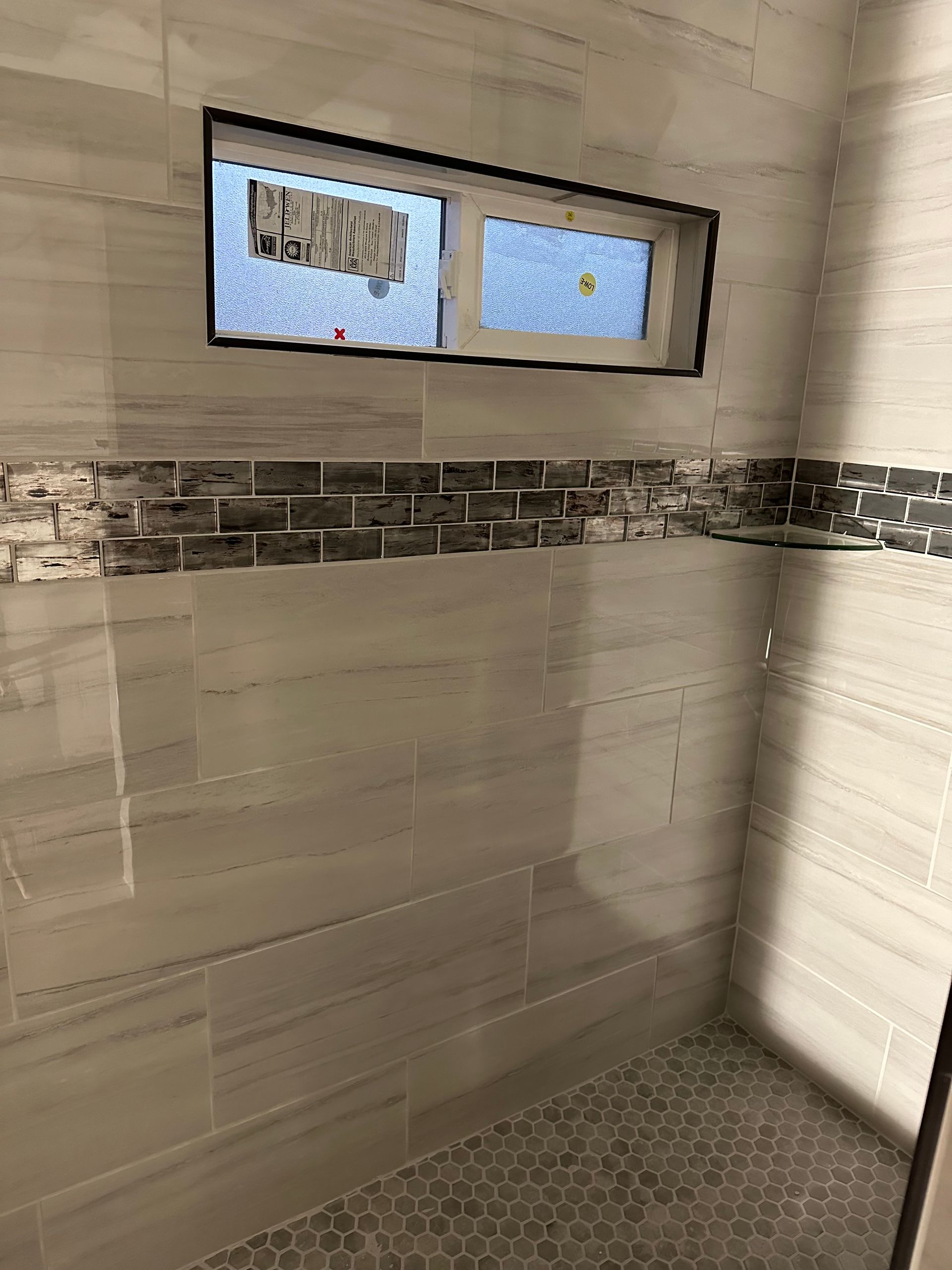 Bathroom shower with beige tile walls, mosaic floor, and two small frosted windows.