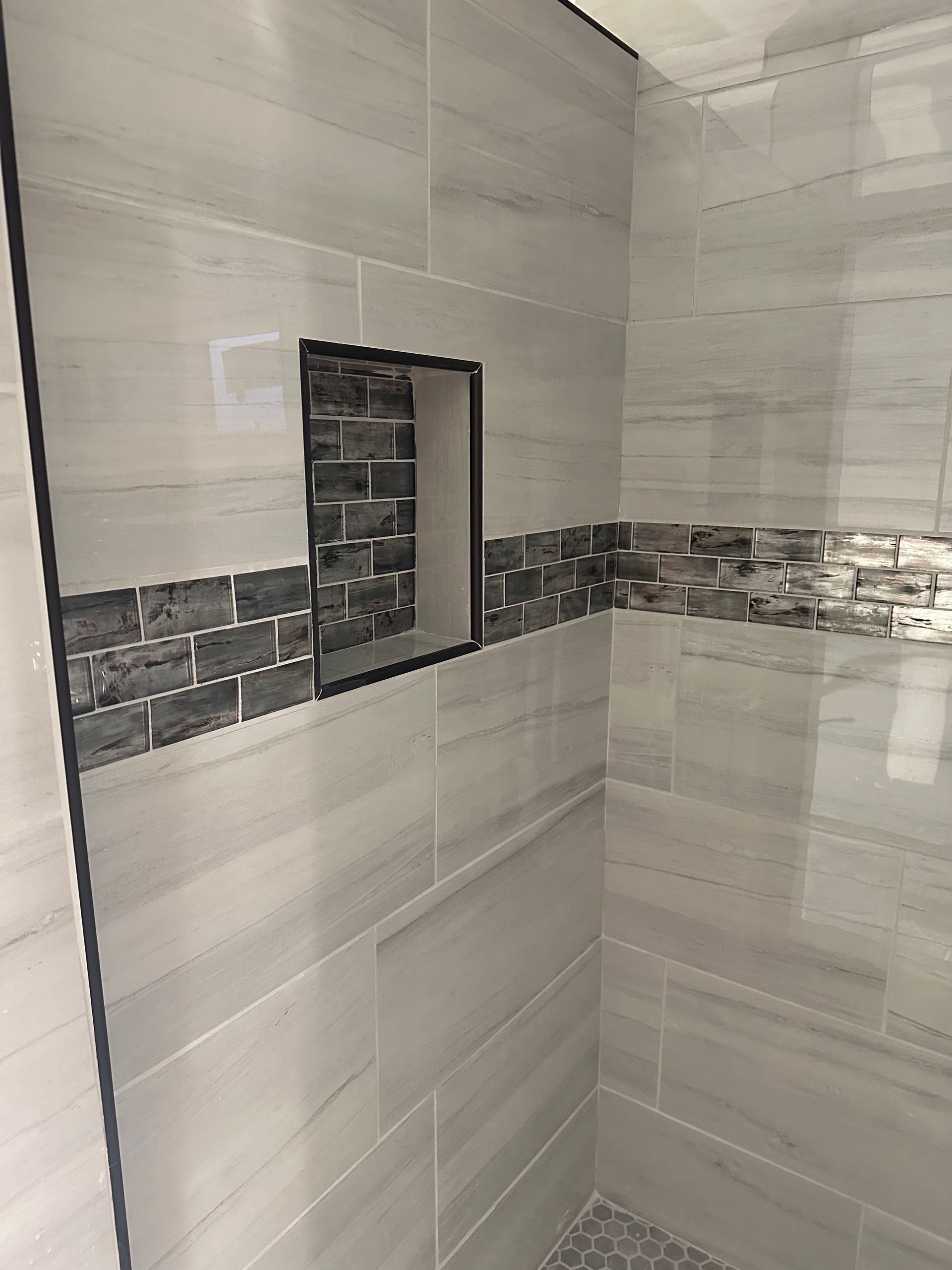 Tiled shower wall with a small recessed niche and horizontal mosaic accent strip