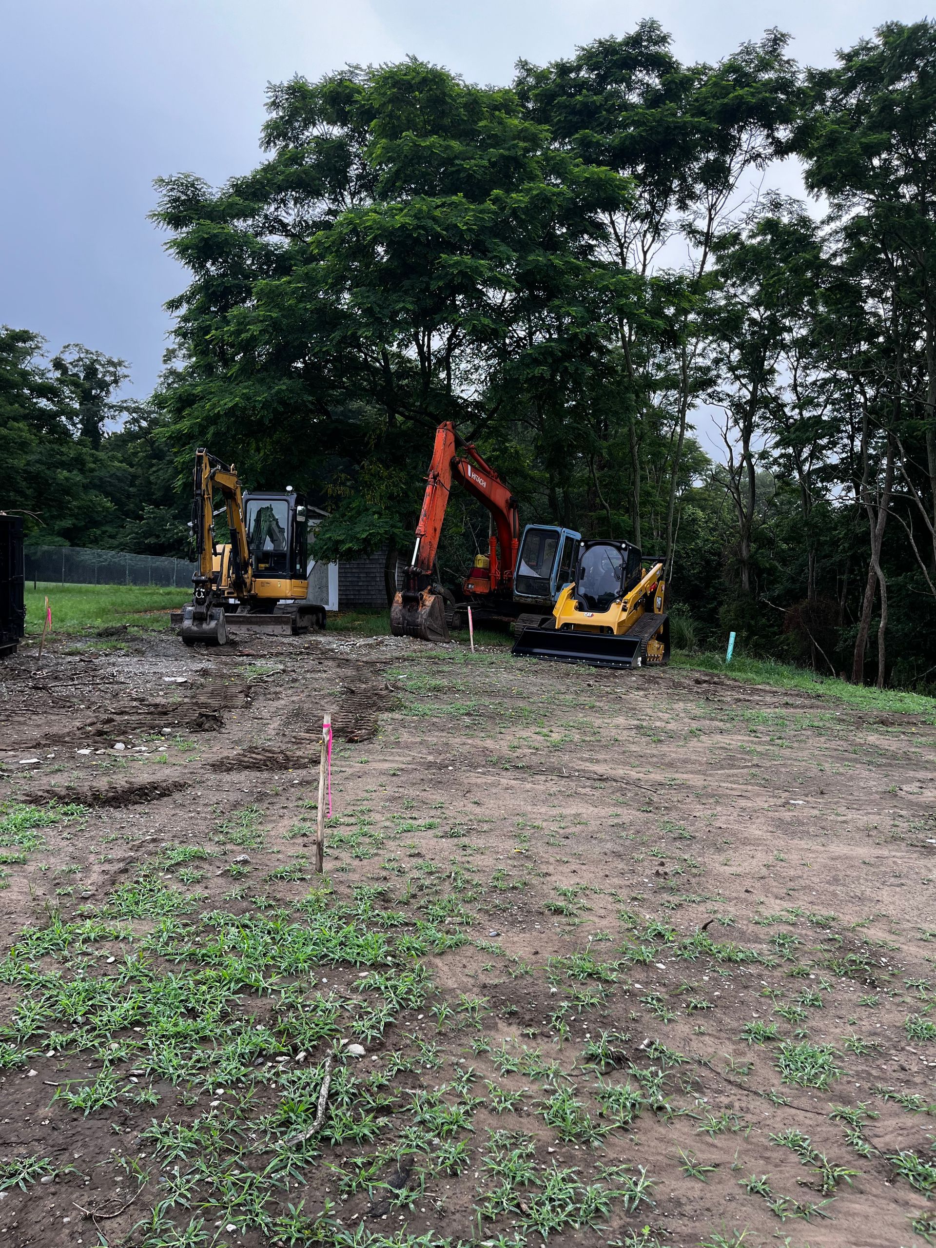 Two excavators are parked in a dirt field with trees in the background.