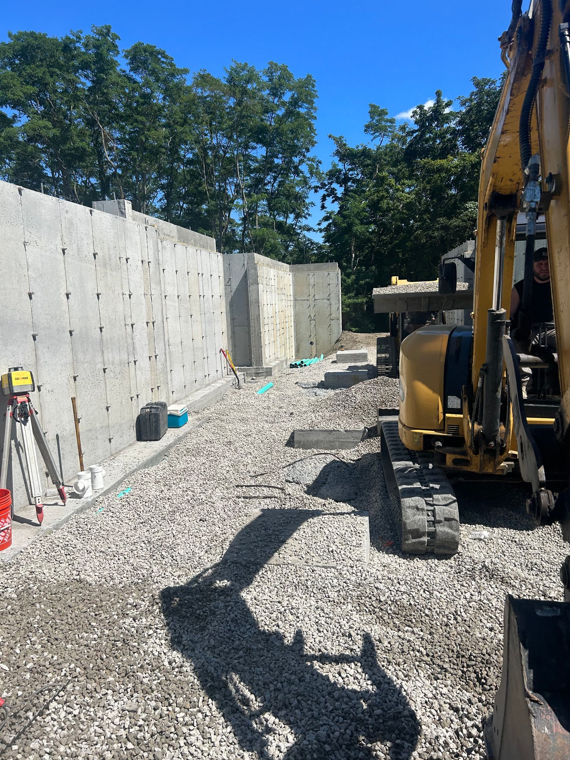 A yellow excavator is sitting on a gravel road next to a concrete wall.