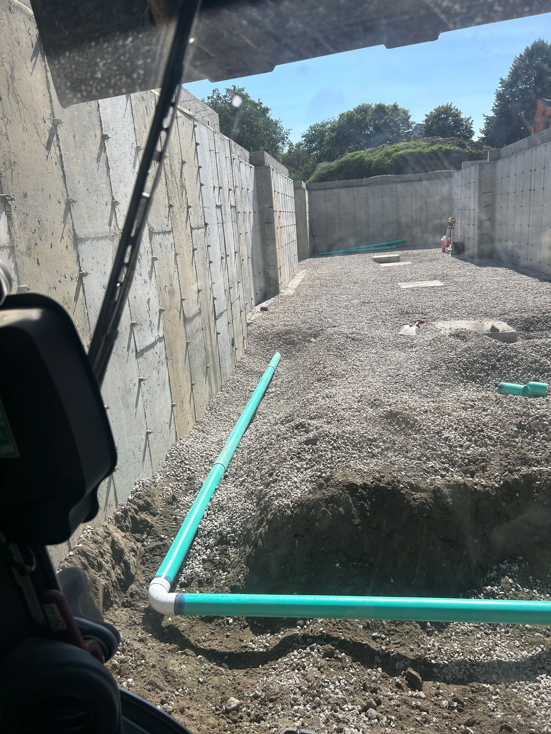 A green pipe is laying in the dirt next to a concrete wall.