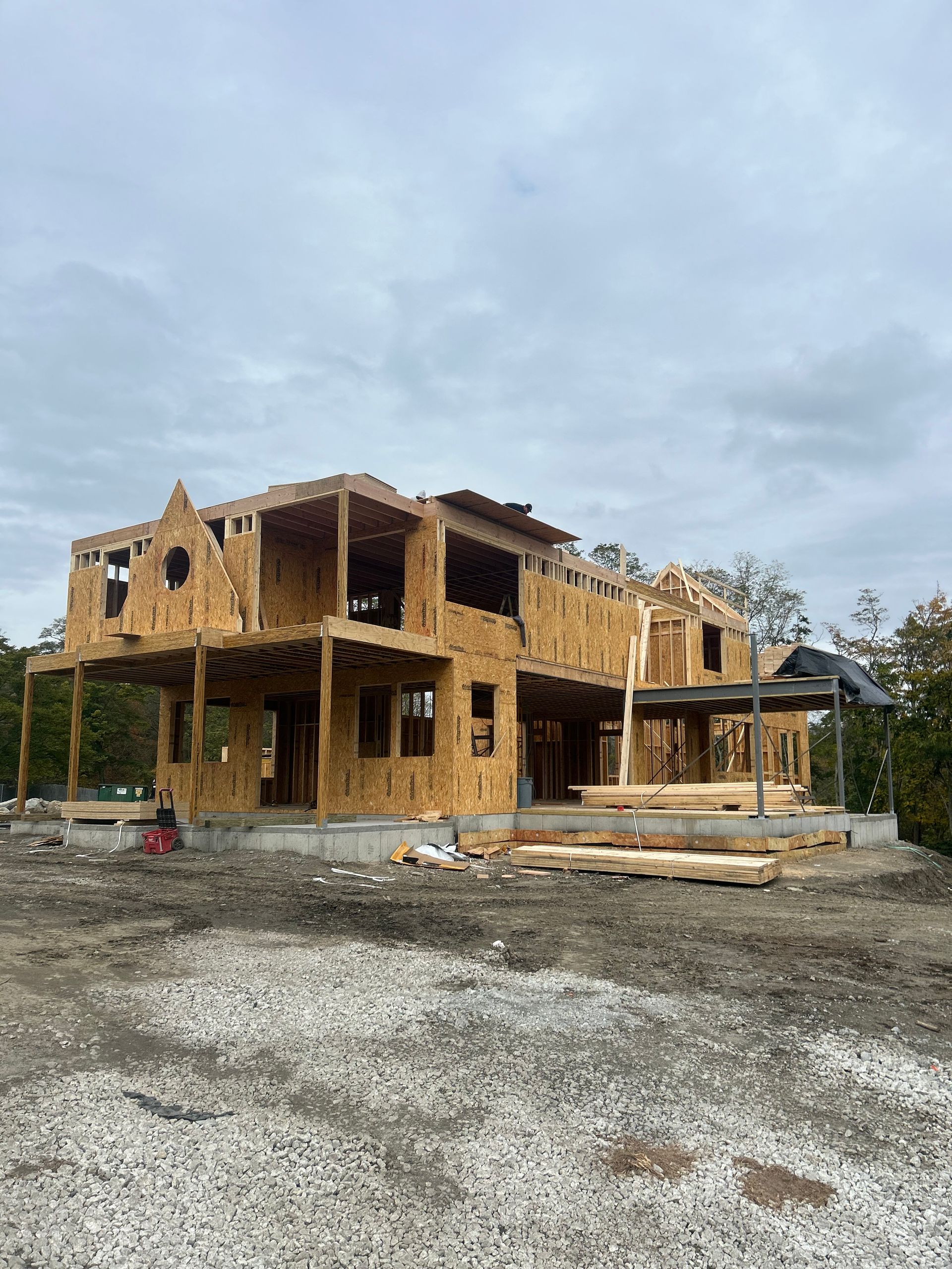 A large wooden house is being built in a gravel lot.